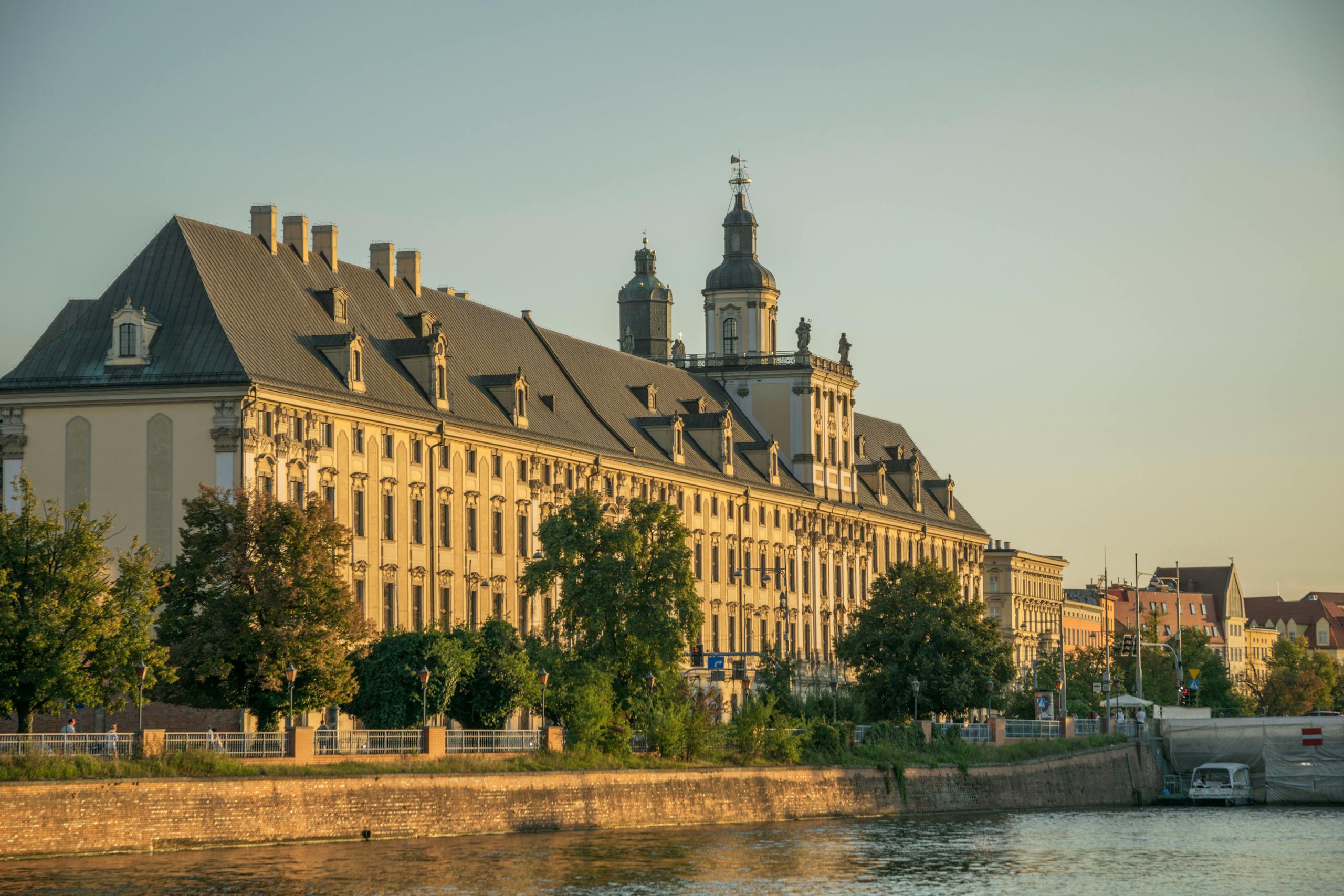 Scenic view of the historic Wrocław University building along the Odra River at sunset.
